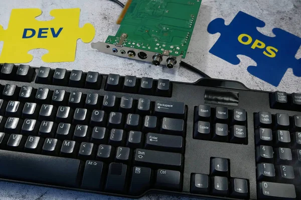 Dev and Ops symbol in hand on motherboard and keyboard background. DevOps Concept for software engineering culture and practice of software development and operation, closeup