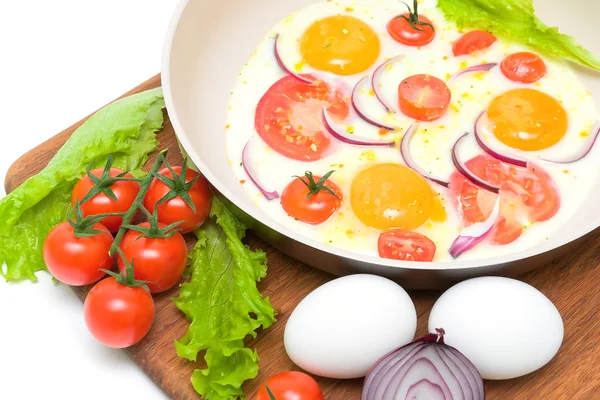 Fried eggs in a frying pan and vegetables on the cutting board — Stock Photo, Image