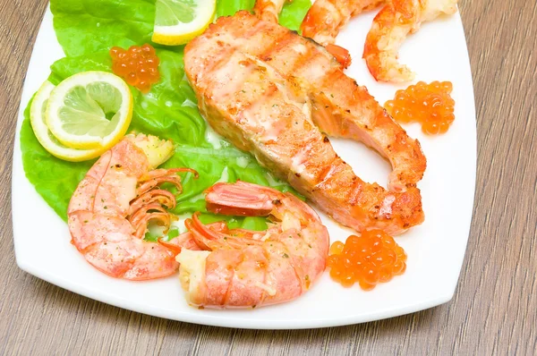 A piece of broiled fish, shrimp and red caviar on white plate cl — Stock Photo, Image