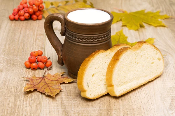 Pão e leite em uma caneca em tábuas de madeira — Fotografia de Stock