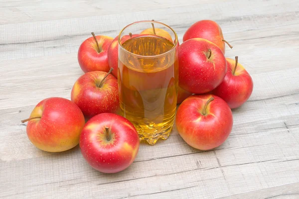 Red apples and glass of apple juice on a wooden table — Stock Photo, Image
