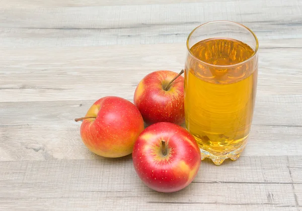 Dojrzałe czerwone jabłka i szklanką soku na drewnianym stołem — Zdjęcie stockowe