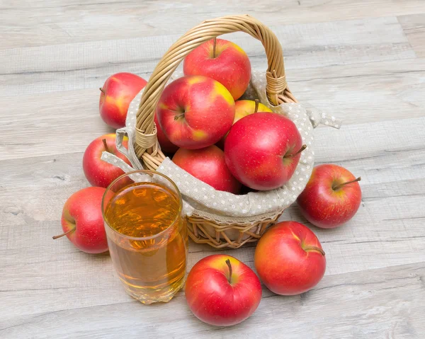 篮子里的苹果和一杯果汁木制的桌子上 — 图库照片