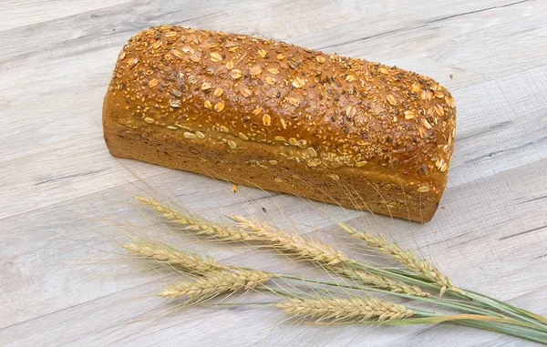 Brood van roggebrood en oren van tarwe op de houten tafel — Stockfoto