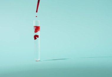 Test tüpü ve pastel mavi arka plan için bir damla kan. Aşı araştırmaları minimum konsept.