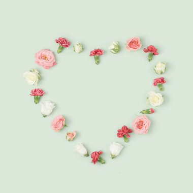 Açık yeşil arka planda çeşitli rengarenk bahar çiçekleri kalp düzeni. Sevgililer Günü Minimum Konsept.