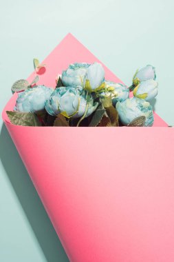 Artificial flowers bouquet wrapped in pink paper on a light blue background. Springtime minimal concept. clipart