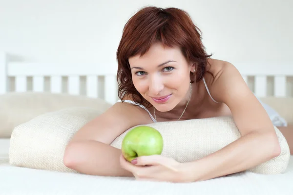 Atrakcyjna młoda kobieta z zielonym jabłkiem w łóżku — Zdjęcie stockowe