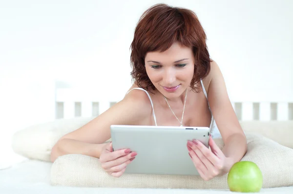 Mujer con una manzana verde y una tableta en la cama leyendo ebook — Foto de Stock