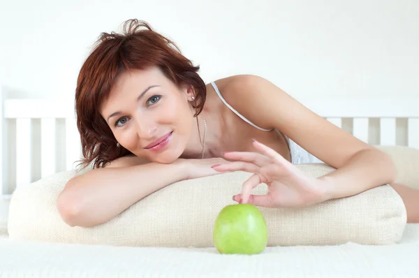 Ελκυστική νεαρή γυναίκα με ένα πράσινο μήλο στο κρεβάτι Εικόνα Αρχείου