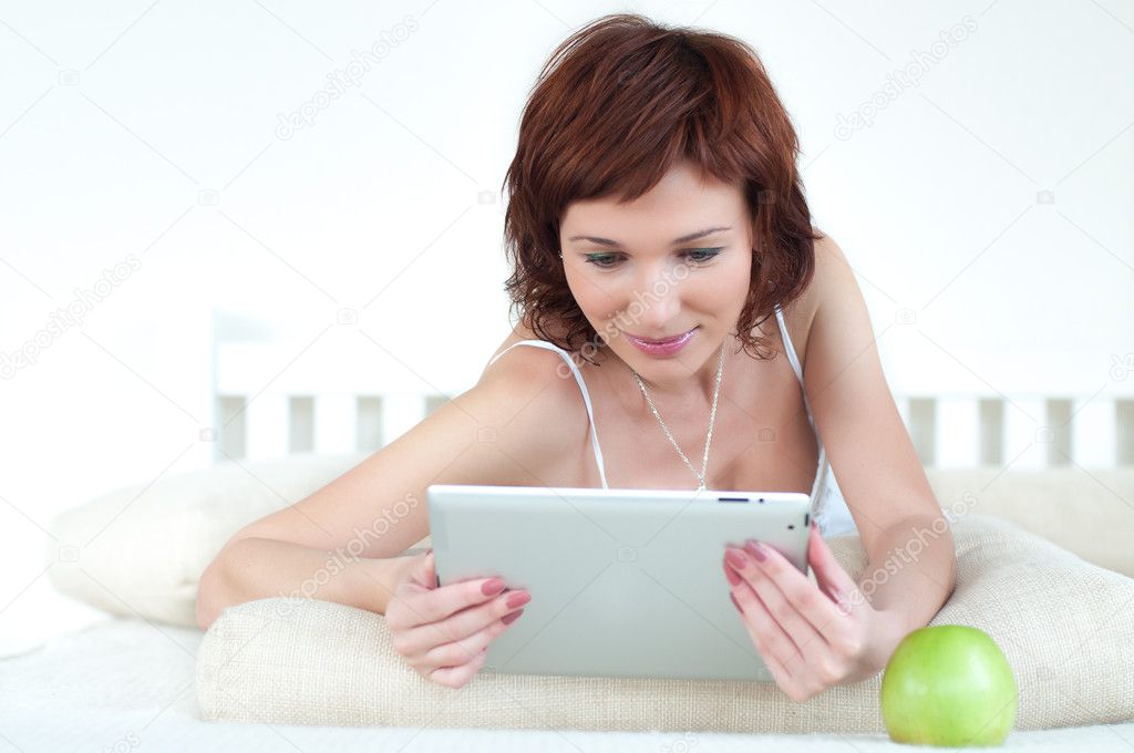 Woman with an green apple and tablet at bed reading ebook