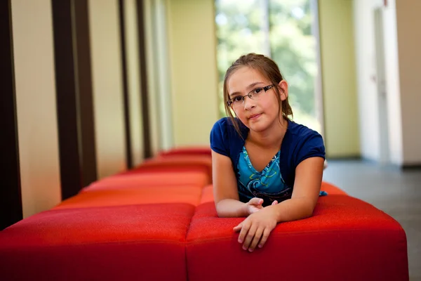 Little girl on a bench in a sunny room — Stock Photo, Image