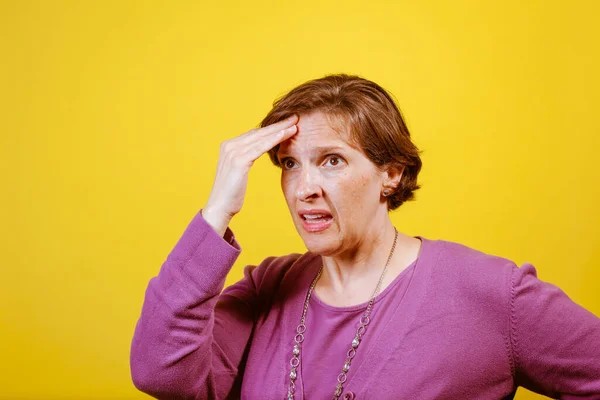 迷人的成熟女人 穿着紫色的衬衫 背景是黄色的 手放在头上 头疼难忍 疼痛管理概念 — 图库照片