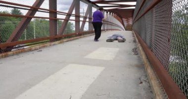 A woman rushes to help a man who fainted on a foot bridge over a busy highway