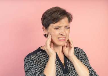 Brunette woman in her 50s in the studio with a pink background with TMJ issues