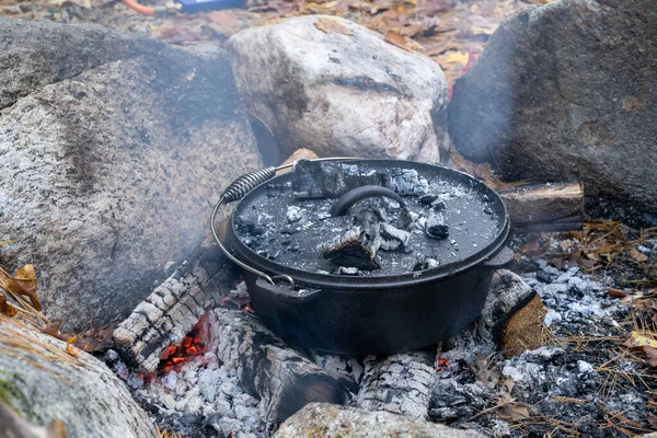 Food baking in a cast iron Dutch Oven outside over a smokey open wood fire on an autumn day