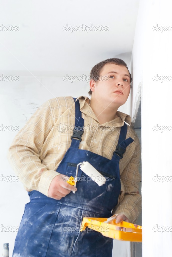 Builder looking at the wall with paint roller in hand.