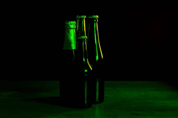 四个啤酒瓶在黑色背景上的轮廓 绿色的灯光照亮了它们的一面 — 图库照片
