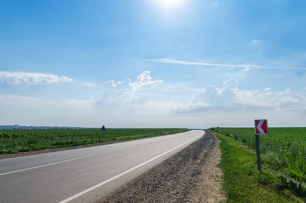 Asphalt road under cloudy sky with sun — Stock Photo, Image