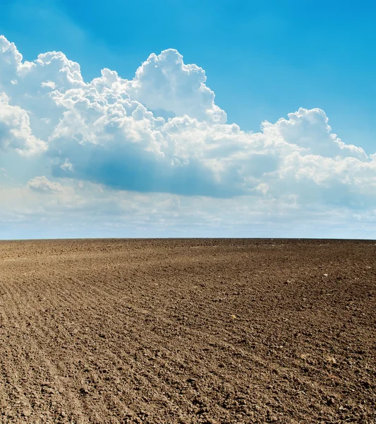 Blauwe bewolkte hemel en zwarte geploegd veld — Stockfoto