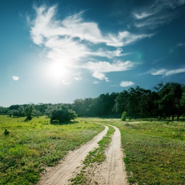 sun and clouds over road to wood