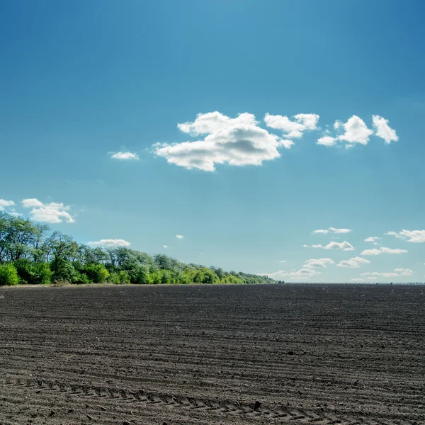 Black field under cloudy blue sky — Stock Photo, Image