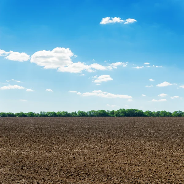 Campo de primavera negro arado y nubes blancas en el cielo azul — Foto de Stock