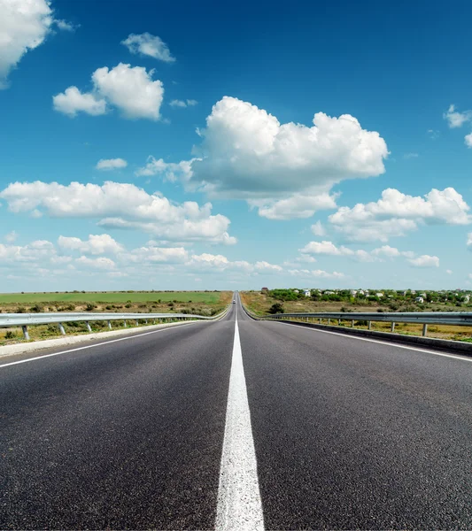 Zwarte asfaltweg tot horizon onder diepblauwe bewolkte hemel — Stockfoto