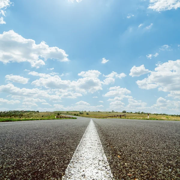 White line on asphalt road under sky with sun and clouds — Stock Photo, Image
