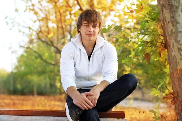 Молодой человек отдыхает на скамейке в парке, снаружи — стоковое фото