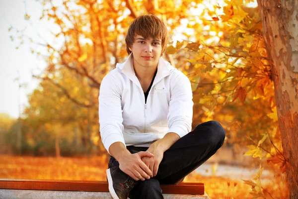 Bankta oturan genç adam sonbahar — Stok fotoğraf