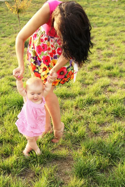 Baby taking first steps with mother help walking in the park — Stock Photo, Image