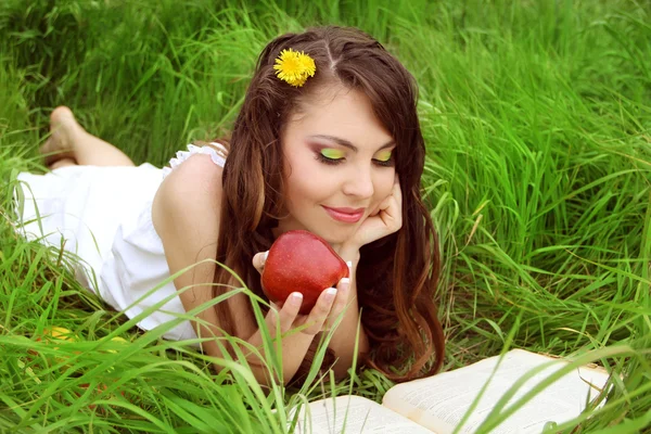 Όμορφη χαμογελαστό νεαρή γυναίκα με κόκκινο μήλο, διαβάζοντας το βιβλίο στο — Φωτογραφία Αρχείου