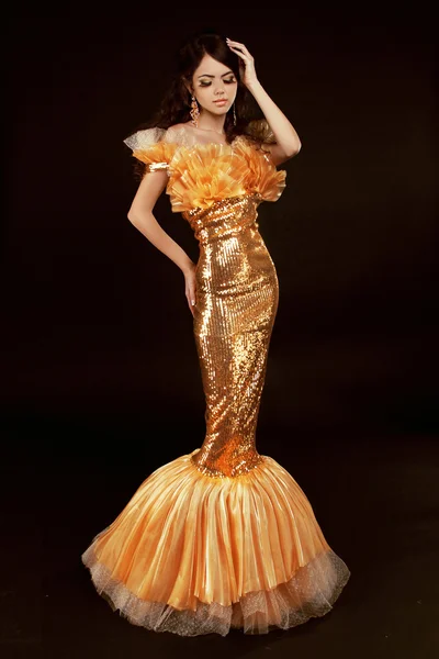 Young brunette lady in golden gorgeous dress posing on black bac — Stock Photo, Image