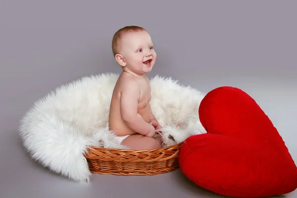 Happy smiling baby with red heart sitting in basket with white f — Stock Photo, Image