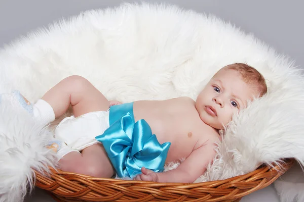 Portrait of Newborn baby lying on fur with blue bow in bed Royalty Free Stock Images