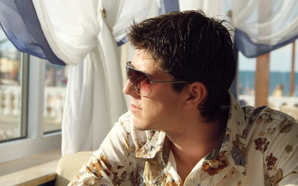 Eleganter junger gutaussehender Mann mit Sonnenbrille, der zum Fenster blickt — Stockfoto