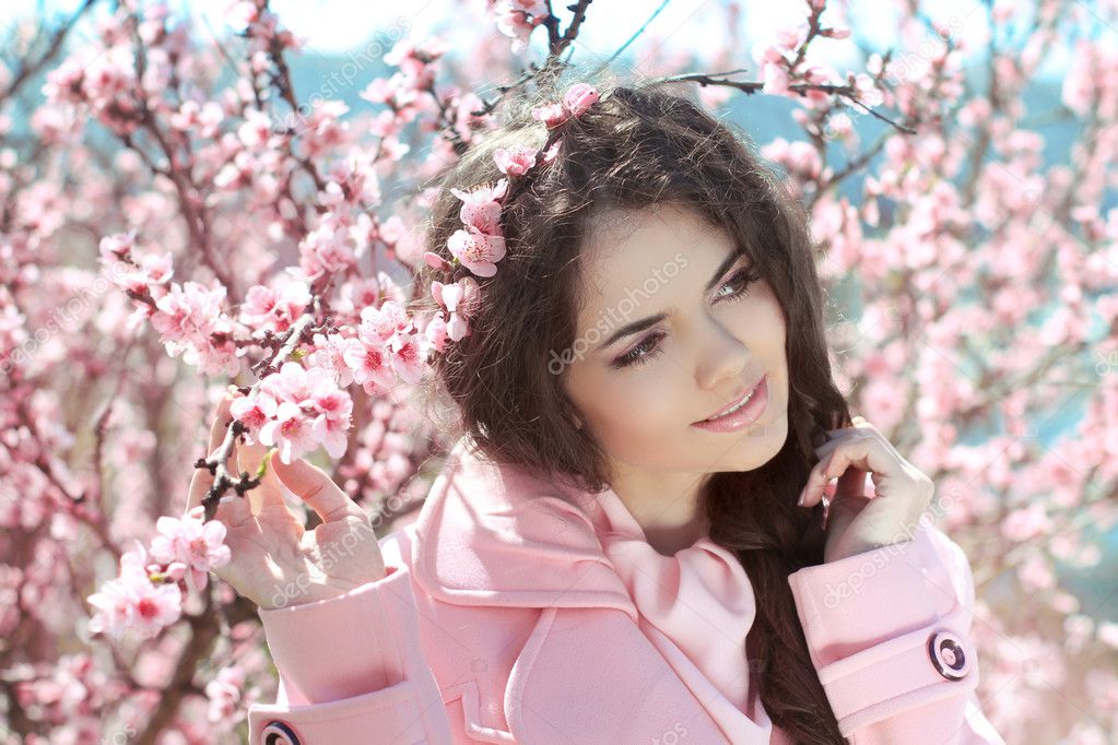 Beautiful young woman over pink blossom tree, outdoors portrait