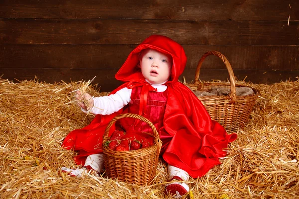 Lustiges Mädchen sitzt auf einem Strohhaufen mit einem Korb. wenig rot — Stockfoto