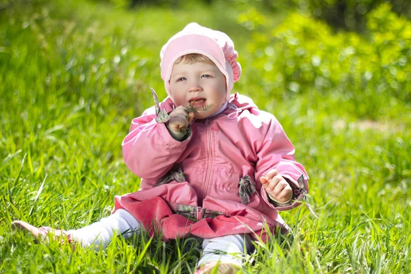 Porträtt av roliga vackra lilla flicka sitter på ett grönt gräs — Stockfoto
