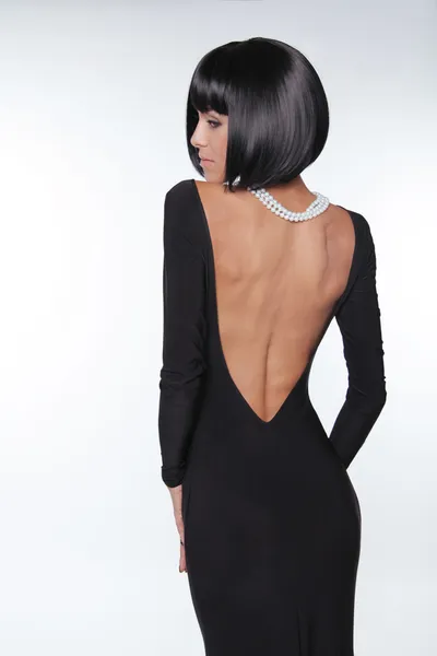 Brunett kvinna med sexiga tillbaka i svart klänning poserar på studio. v — Stockfoto