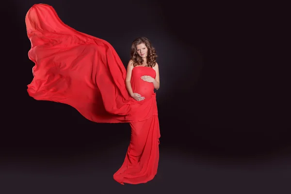 Beautiful Pregnant woman stroking her belly with red blowing tis — Stock Photo, Image