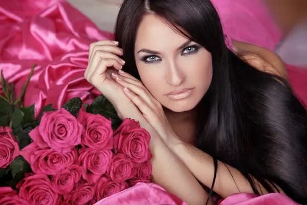 Beauty portrait of brunette girl with pink Roses lying on the be — Stock Photo, Image