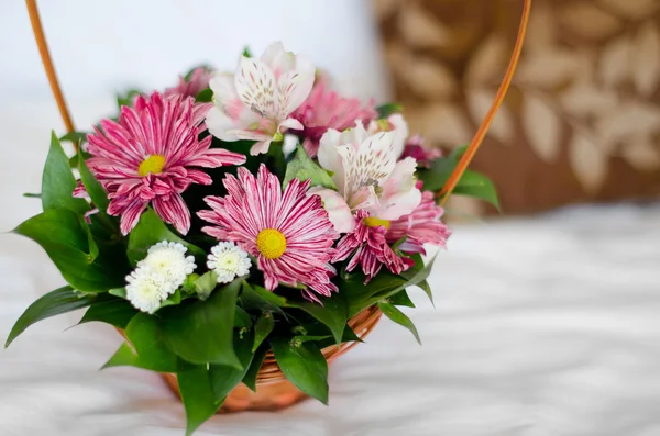 Mooi boeket van kleurrijke bloemen in mand tegen het bed — Stockfoto