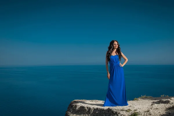 Schöne Frau steht auf einer Klippe über blauem Himmel. brünettes Mädchen — Stockfoto