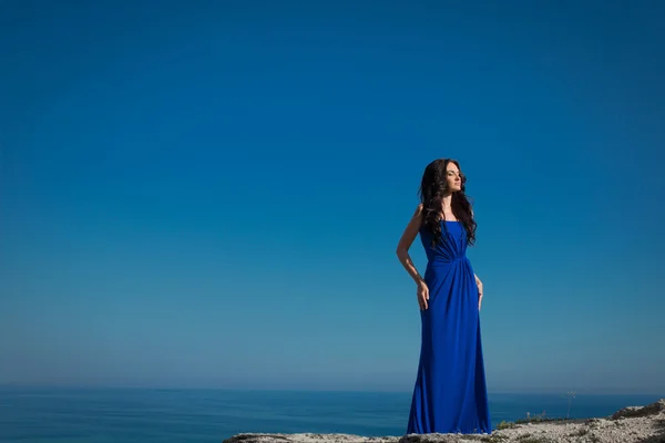 Beautiful woman standing on a cliff over blue sky. Brunette girl — Stock Photo, Image