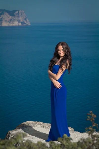 美丽的女人站在悬崖上，在蓝蓝的天空。黑发的女孩 — 图库照片