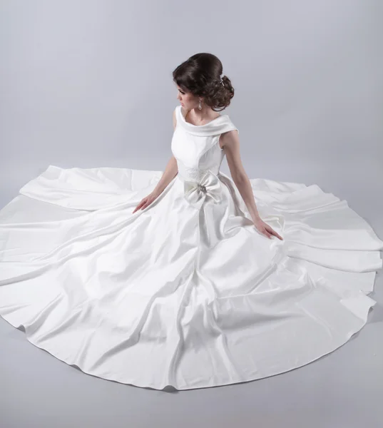 Beautiful charming bride in a luxurious dress sitting over gray — Stock Photo, Image