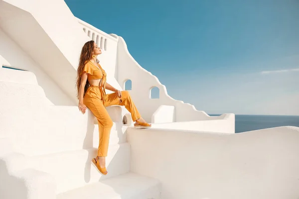 サントリーニ島ギリシャにポーズ夏休みに黄色の服の美しい女の子モデル エーゲ海の上の白いバルコニーの美しい女性のファッション屋外写真 — ストック写真