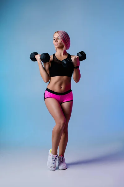 文雅的运动背景 身强体壮的现代女子带着强壮肌肉的哑铃进行锻炼 蓝色健身霓虹灯横幅 健身馆 女强人穿运动服 粉色头发 — 图库照片